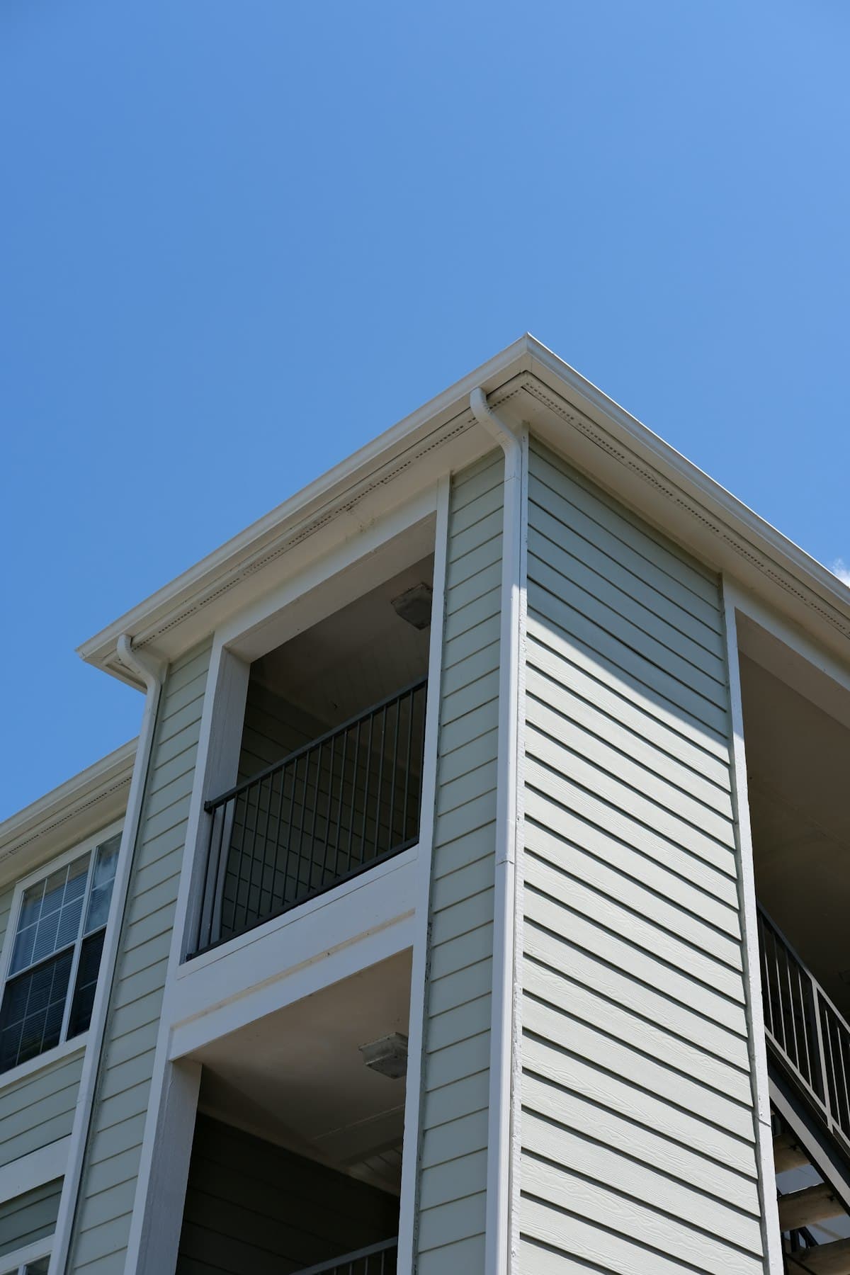 The corner of a pale, clapboard-clad residential building with covered balconies, against a clear blue sky.
