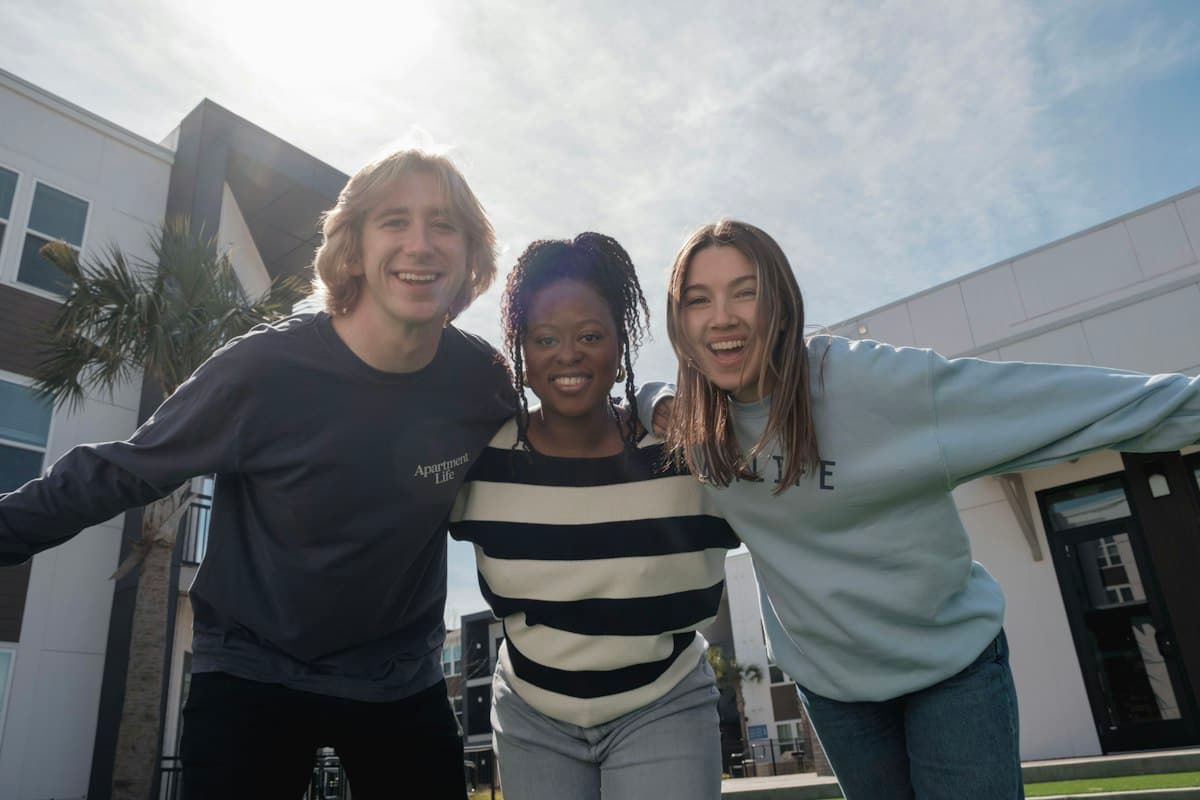 Three students standing together with their arms around each other, smiling.